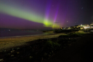 The image is of a beach with houses and a rainbow in the sky. northern lights Lossiemouth Scotland.