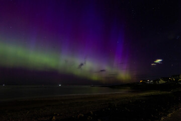 The image is of a beach with houses and a rainbow in the sky. northern lights Lossiemouth Scotland.
