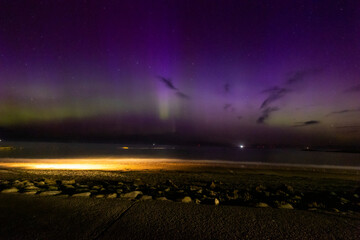 The image is of a beach with houses and a rainbow in the sky. northern lights Lossiemouth Scotland.