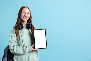 Jolly young girl laughing while presenting tablet with isolated screen display, blue studio...
