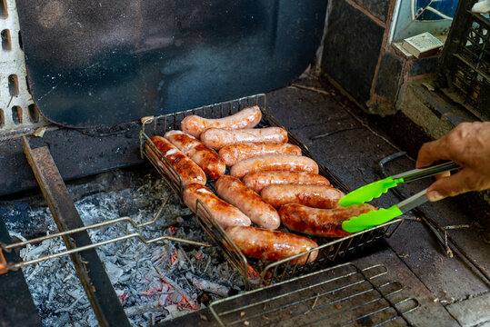 Anonymous person frying sausages on a charcoal grill. Street food.