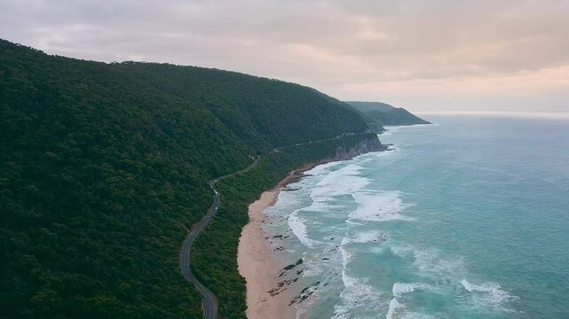 4K drone video of a camper van driving along a stunning long road next to a beautiful beach in Esperance, Western Australia. White waves from the blue ocean are crashing against the white sand beach.