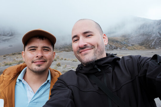 Two Latino men taking a selfie amidst a mountainous landscape