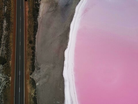 Aerial view of a pink lake and the road next to the road 