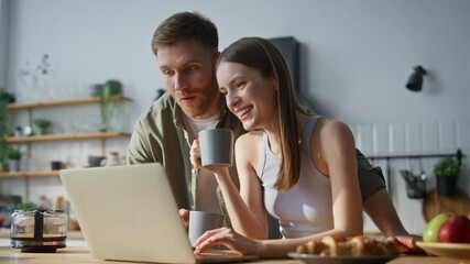 Talking couple browsing laptop website drinking coffee in kitchen closeup.  - Powered by Adobe