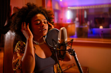 Diverse vocalist with headphones singing a song into mic at music studio