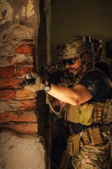 Portrait of air soft player aiming with rifle from ambush in ruins.