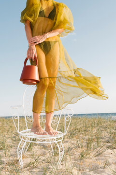 Woman in Sheer Dress Standing on Chair at Beach