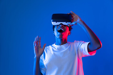 Surprised young African American looking through VR holding interesting object hologram on pink...