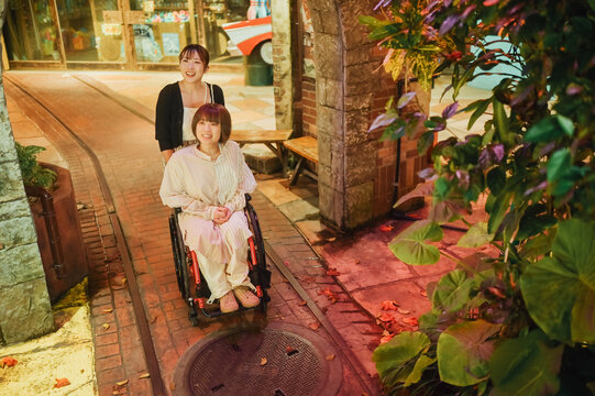 車椅子に乗った日本人女性が友人の女性と夏の夜の沖縄を旅を満喫している