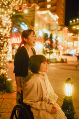 車椅子に乗った日本人女性が友人の女性と夏の夜の沖縄を旅を満喫している