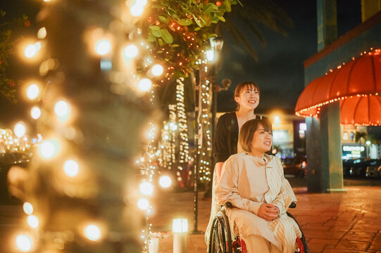 車椅子に乗った日本人女性が友人の女性と夏の夜の沖縄を旅を満喫している