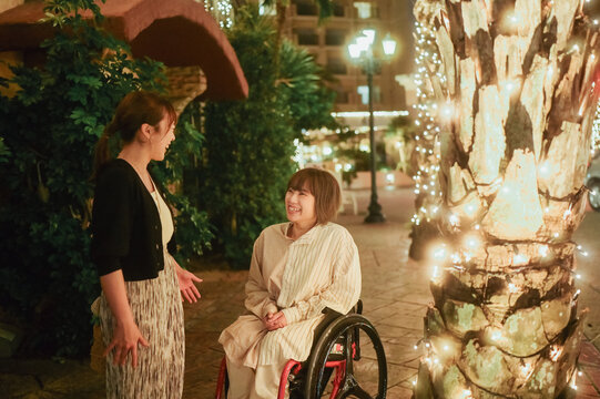 車椅子に乗った日本人女性が友人の女性と夏の夜の沖縄を旅を満喫している