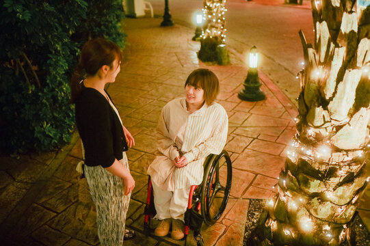 車椅子に乗った日本人女性が友人の女性と夏の夜の沖縄を旅を満喫している