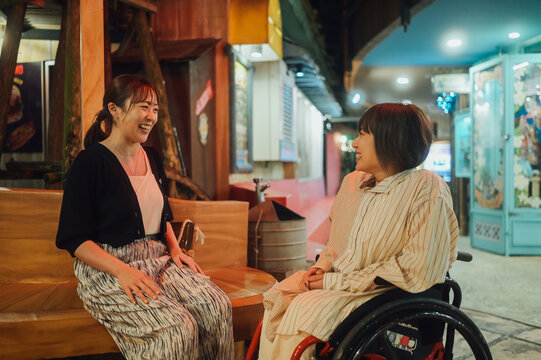 車椅子に乗った日本人女性が友人の女性と夏の夜の沖縄を旅を満喫している