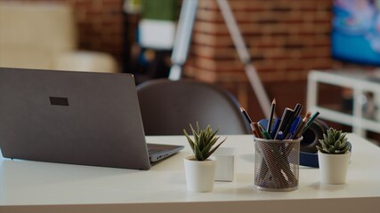 Laptop on desk next to mini house plants in cozy stylish empty apartment, panning shot. Notebook placed on wooden table in bright modern living room with brick walls and nice interior design, close up