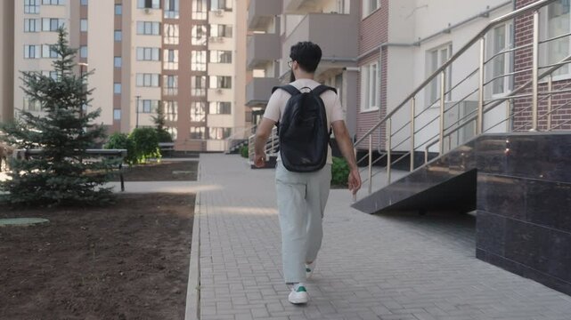 A young man with glasses and a black backpack walks down the outdoor stairs of an apartment building.