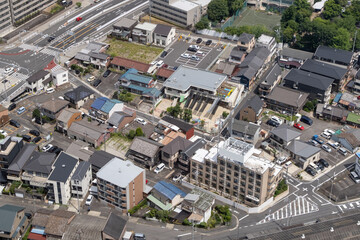 Aerial view of a populated Japanese urban neighborhood with apartment buildings, homes, houses, and childcare center. Roads and parking lots crisscross, a complex street network. Nagoya, Japan