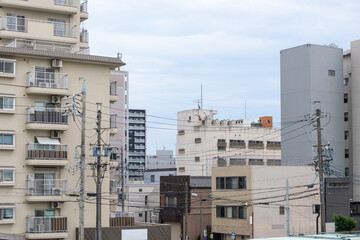 A typical urban cityscape in Nagoya, Japan, densely packed apartment buildings and a network of electrical wires crisscrossing overhead. A populated city neighborhood with many homes and balconies.