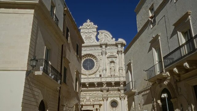 Baroque architecture of santa croce basilica in lecce, puglia, framed by historic buildings under a clear blue sky.