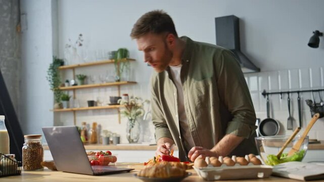Guy watching video recipe chopping vegetables in kitchen. Guy slicing red pepper