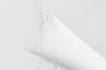 Close-up of a stream of water pouring on a white mockup of tube of cream with splashes on isolated...