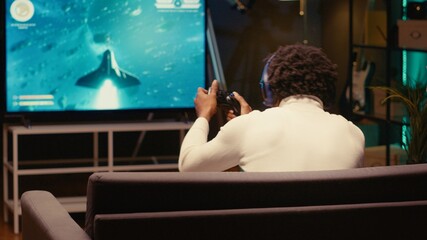 Player in home theatre enjoys game with spaceship shooting laser streams using crosshair overlay to hit enemies. Ray tracing graphics and high FPS SF videogame displayed using video projector