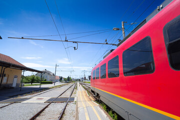 Naklejka premium Slovenian electric train entering Skofja Loka station on a clear day. The modern red train reflects the robust public transportation infrastructure of Slovenia.