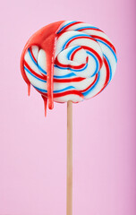 Colored lolly pop on a pink background with syrup running down it.