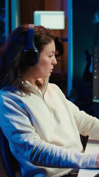 Vertical video Woman listening music while doing software quality assurance, reading source code on computer screen. Developer wearing headphones enjoying podcasts and inspecting coding on desktop PC