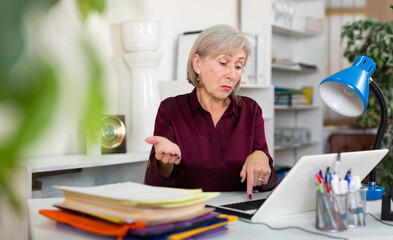 Stressed senior woman working in office, overwhelmed with computer work