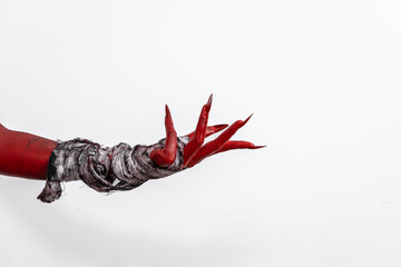 A terrifying red demon hand wrapped in a shroud, reaching out menacingly on a white studio background. This eerie, Halloween-themed image evokes fear and horror with its ghostly, undead appearance.