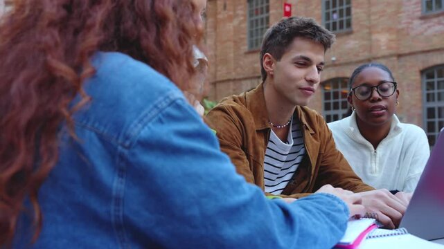 A group of students with laptops sit near the campus and communicate.