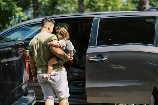 lgbtq woman and mother getting her toddler daughter into car seat