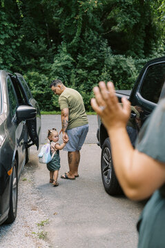 mom waving goodbye to wife and toddler daughter in driveway