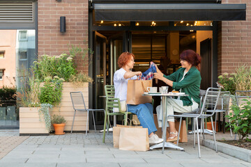 Two Women Unpacking Shopping Bags at Outdoor Cafe
