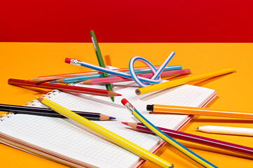 Various colorful pencils on white notebook on red and orange Backdrop