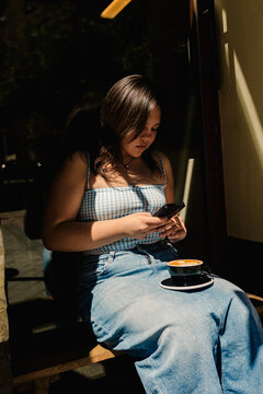 Curvy lady photographs a latte with her smartphone outside a cafeteria