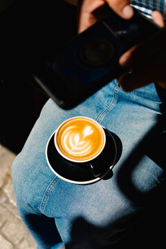 Woman taking a photo of latte art with the cup resting on her lap