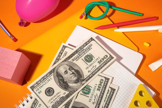 Colorful Pencils, Dollars and Notebooks on Orange Backdrop. 