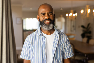Obraz premium Smiling african american senior man in casual shirt standing in home, looking confident
