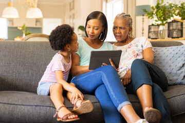 Using tablet, multi-generational family sitting on couch, engaging in conversation