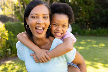 Smiling mother giving piggyback ride to daughter, enjoying time together outdoors