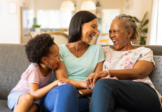 Laughing together, three generations of women bonding on couch at home