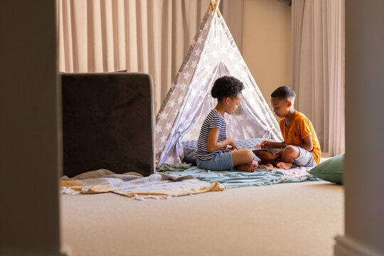 Playing together, two young brother and sister sitting in front of teepee tent indoors, copy space - Powered by Adobe