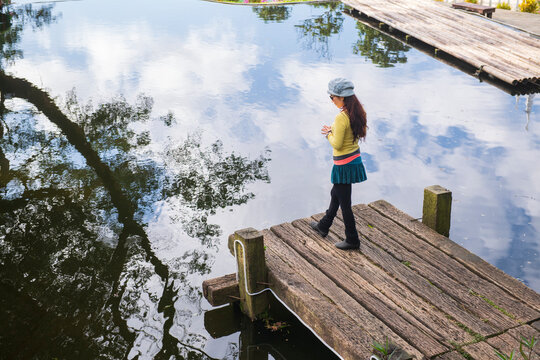 Female stands on dock and  looks at the sky reflection in water