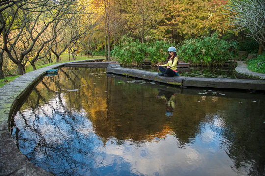 Zen meditation, woman sits near pond surrounded by autumn trees