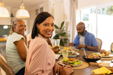 Enjoying family meal, woman smiling at camera while others eat at dining table