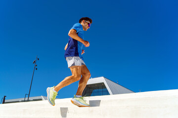 A man in athletic wear runs up white steps under a clear blue sky, exuding energy and determination.