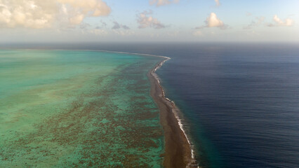Exotic tropical coast line with coral reef and different shades of blue azure ocean water near the island of Taha'a in French Polynesia. Aerial view captured by drone.